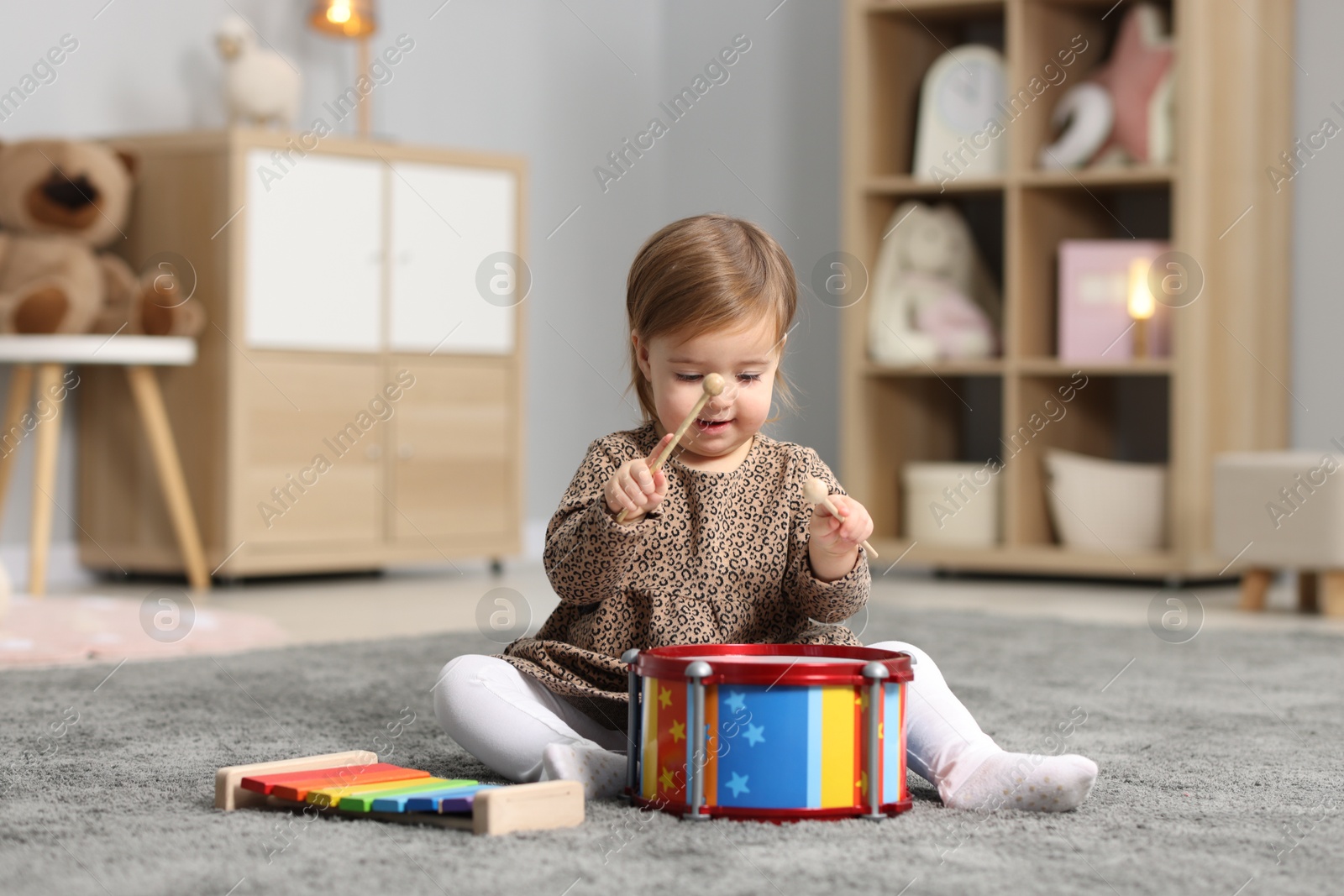 Photo of Cute little girl playing with toy drum on floor at home