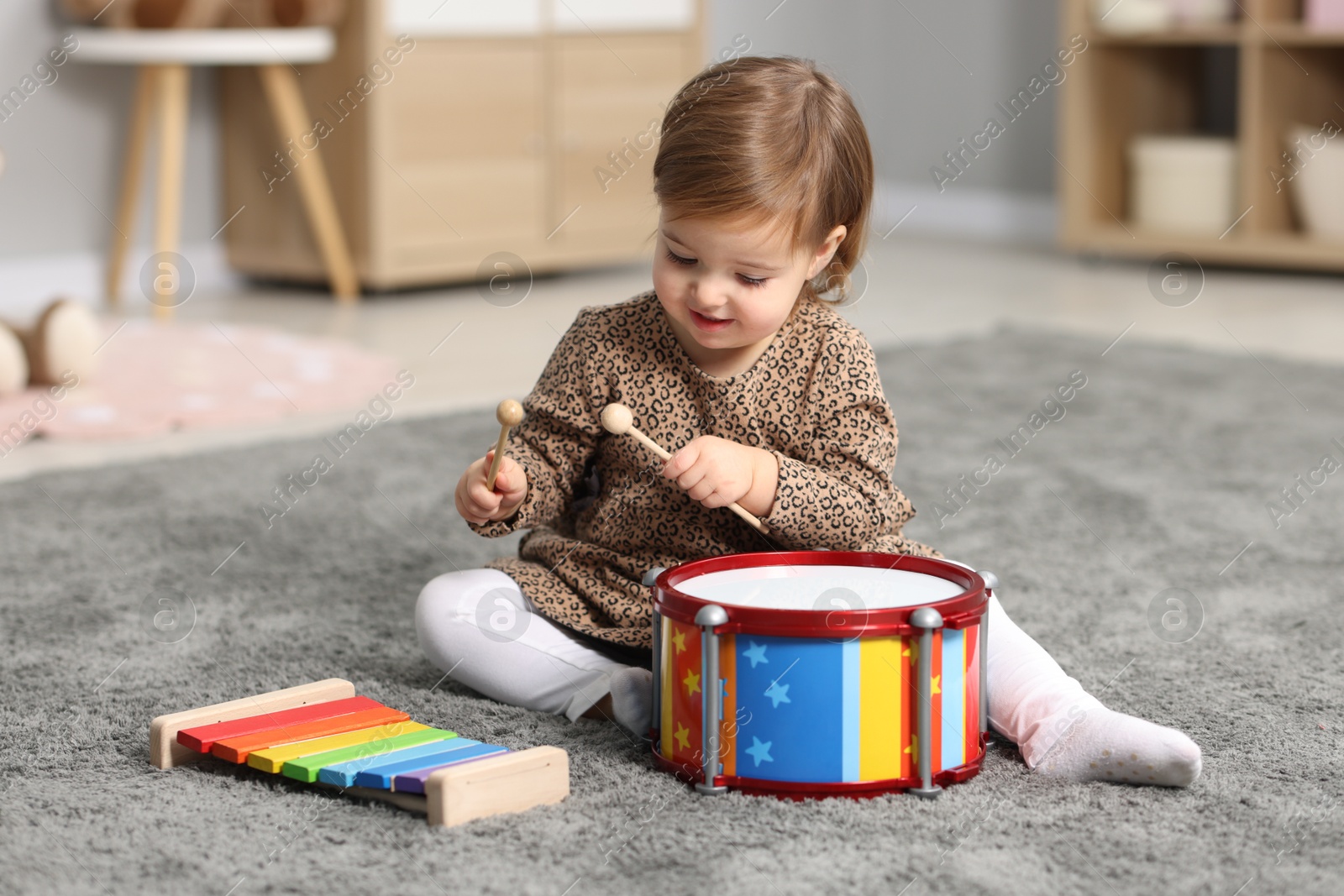 Photo of Cute little girl playing with toy musical instruments on floor at home