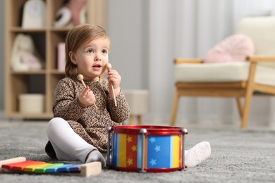 Photo of Cute little girl with toy musical instruments on floor at home, space for text