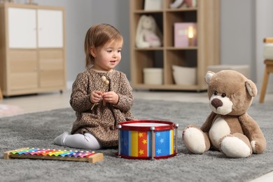 Photo of Cute little girl playing with toy musical instruments on floor at home