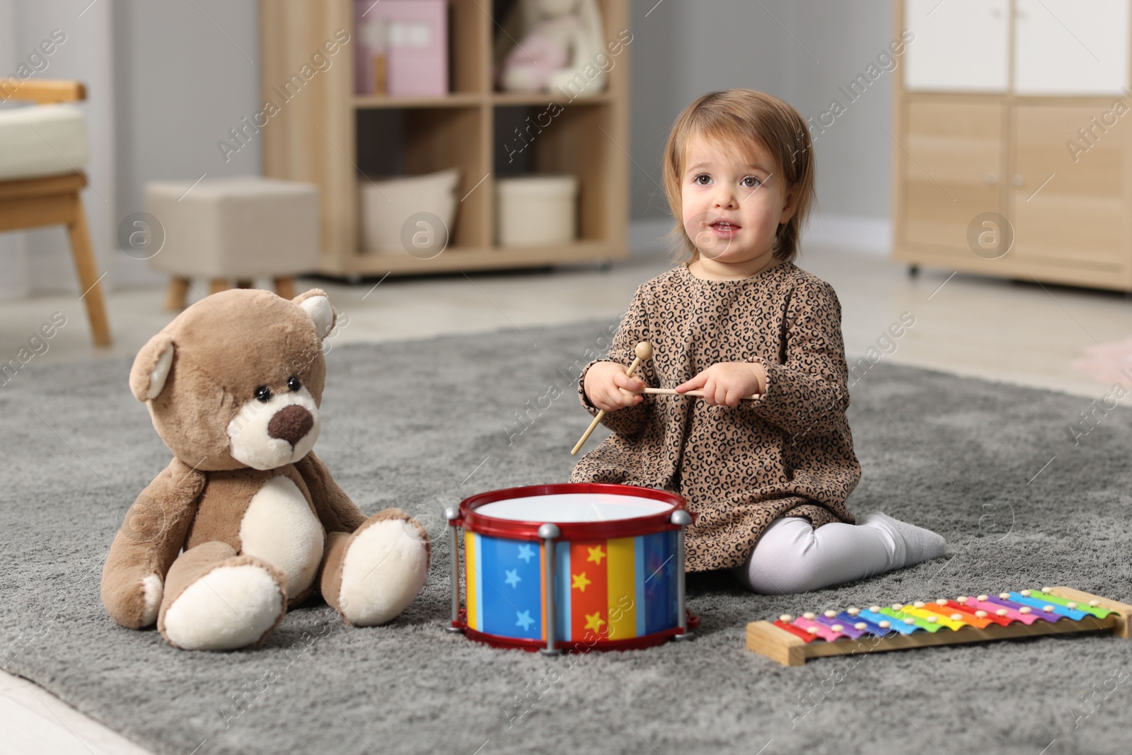 Photo of Cute little girl playing with toy musical instruments on floor at home