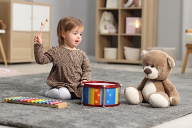 Photo of Cute little girl playing with toy musical instruments on floor at home