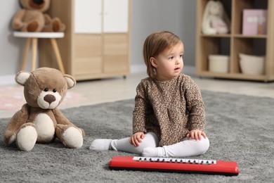 Photo of Cute little girl playing with toy piano at home