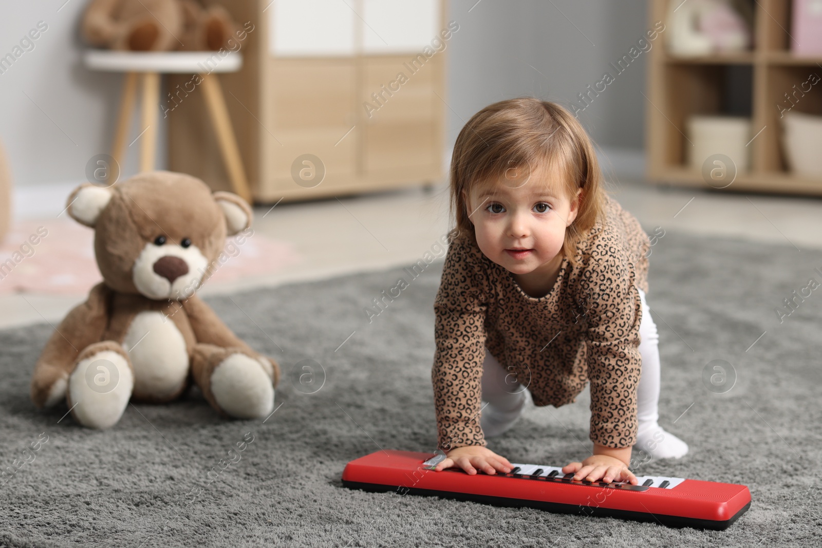 Photo of Cute little girl playing with toy piano at home