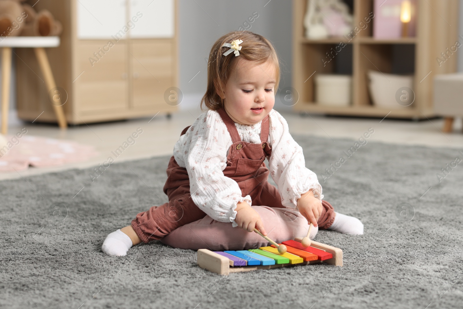 Photo of Cute little girl playing with toy xylophone on floor at home