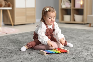 Photo of Cute little girl playing with toy xylophone on floor at home