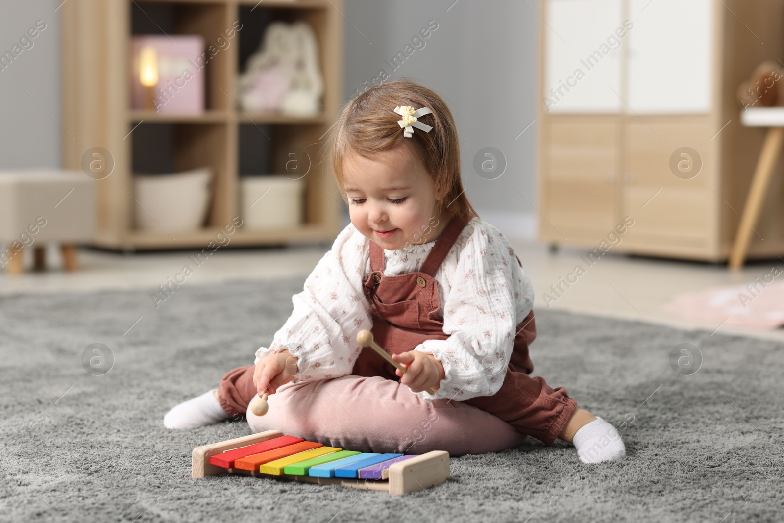 Photo of Cute little girl playing with toy xylophone on floor at home