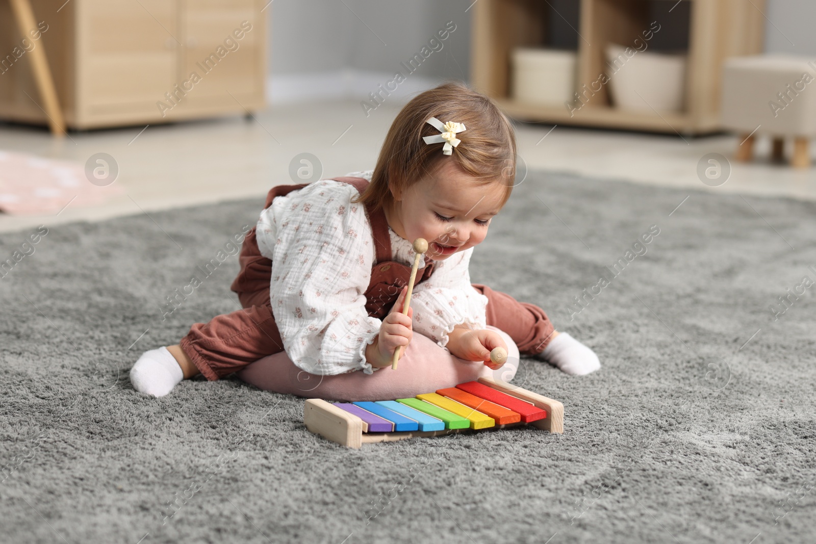 Photo of Cute little girl playing with toy xylophone on floor at home