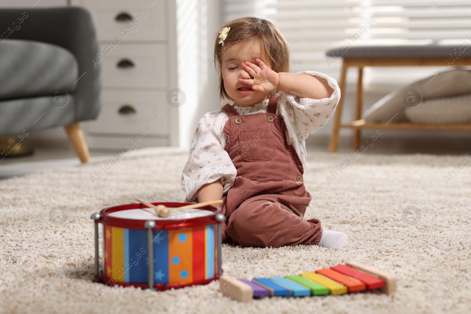 Photo of Cute little girl with toy musical instruments on floor at home