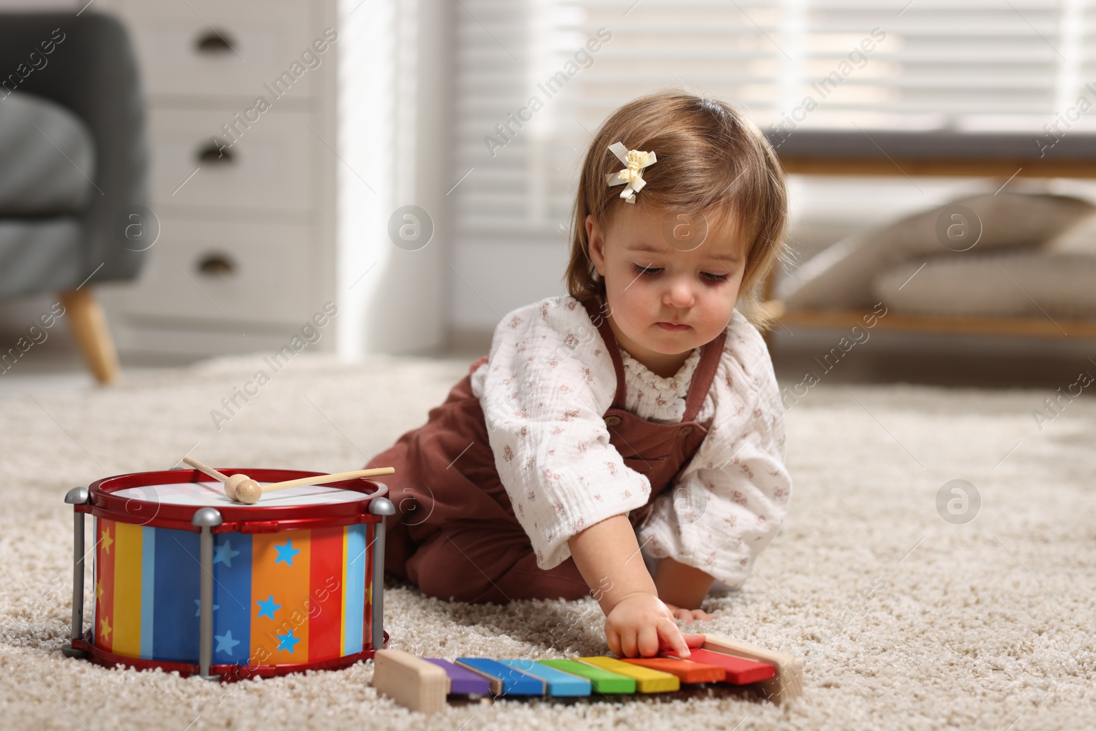 Photo of Cute little girl playing with toy xylophone on floor at home