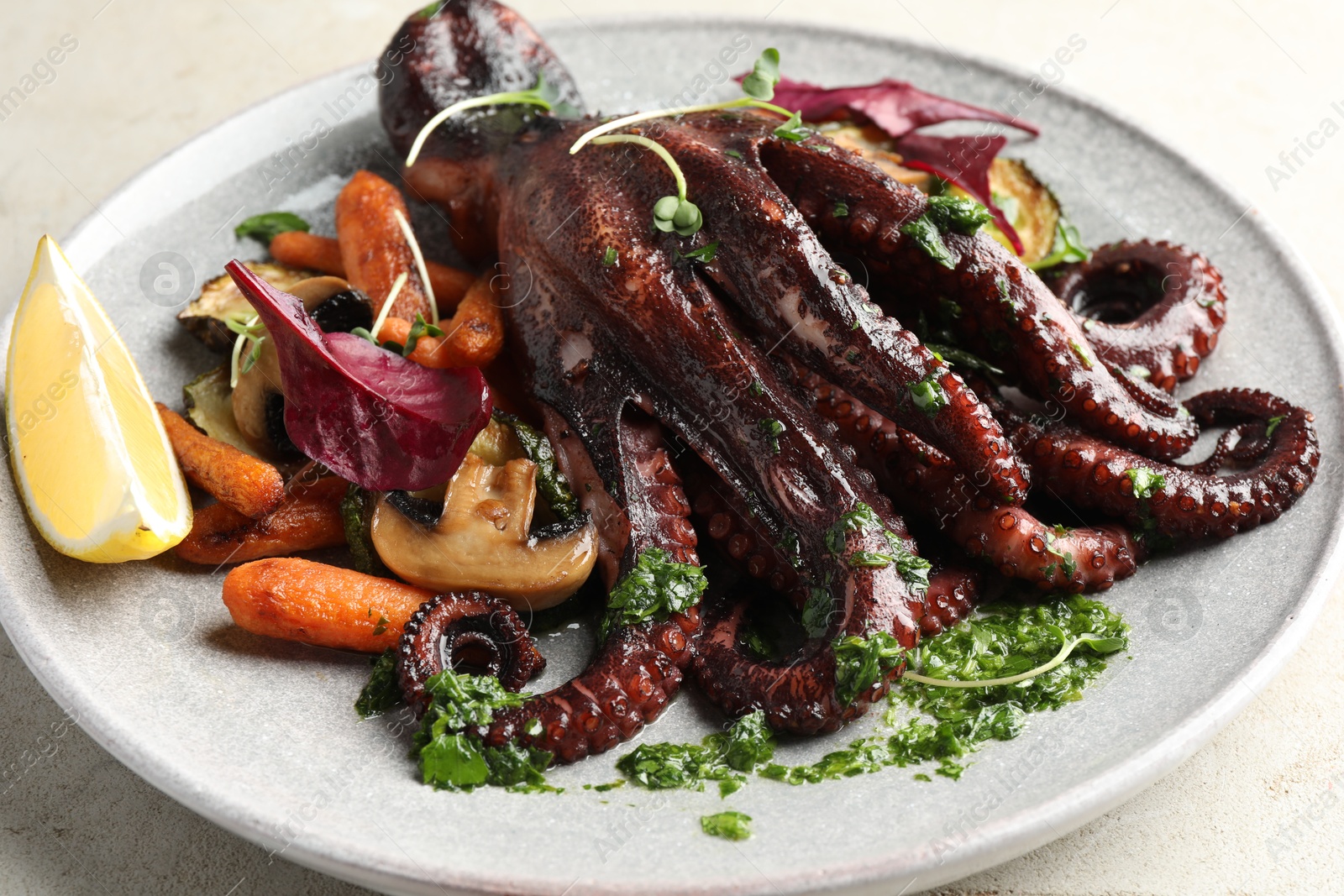 Photo of Roasted octopus with vegetables and mushrooms on light grey table, closeup