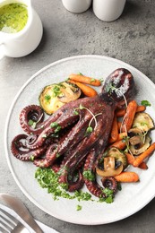 Photo of Roasted octopus served with vegetables and mushrooms on grey table, flat lay