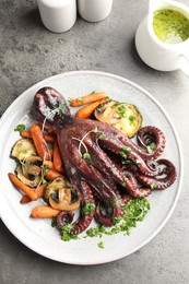 Photo of Roasted octopus served with vegetables and mushrooms on grey table, flat lay