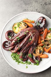 Photo of Roasted octopus with vegetables and mushrooms on grey table, top view