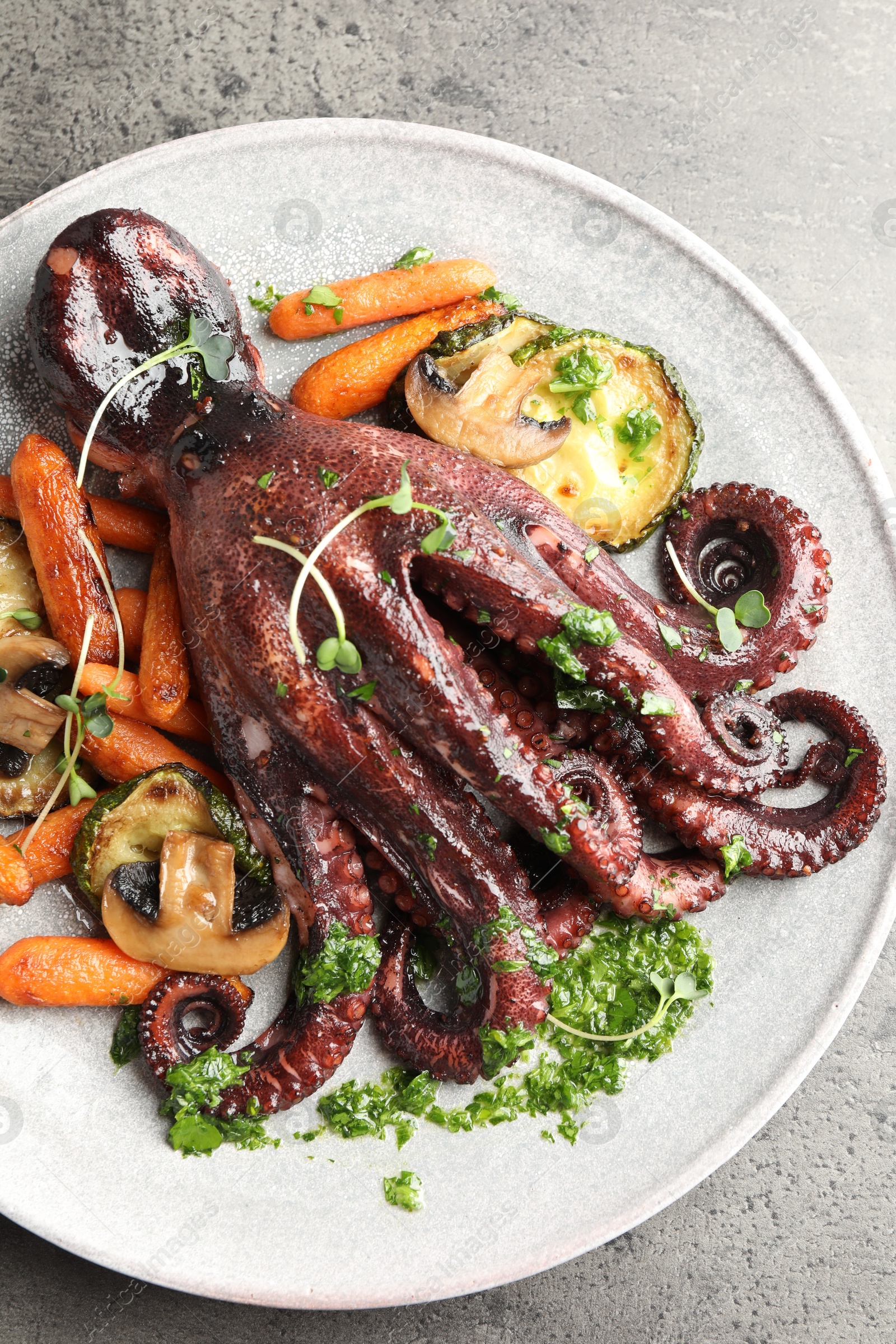 Photo of Roasted octopus with vegetables and mushrooms on grey table, top view