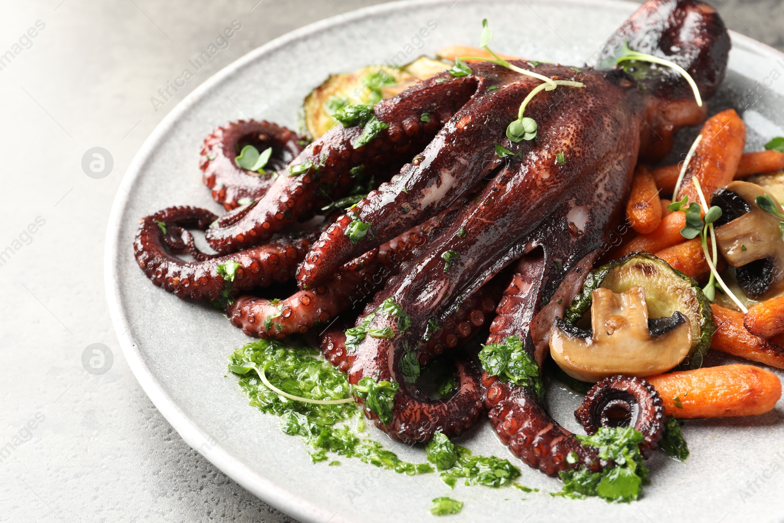 Photo of Roasted octopus with vegetables and mushrooms on grey table, closeup