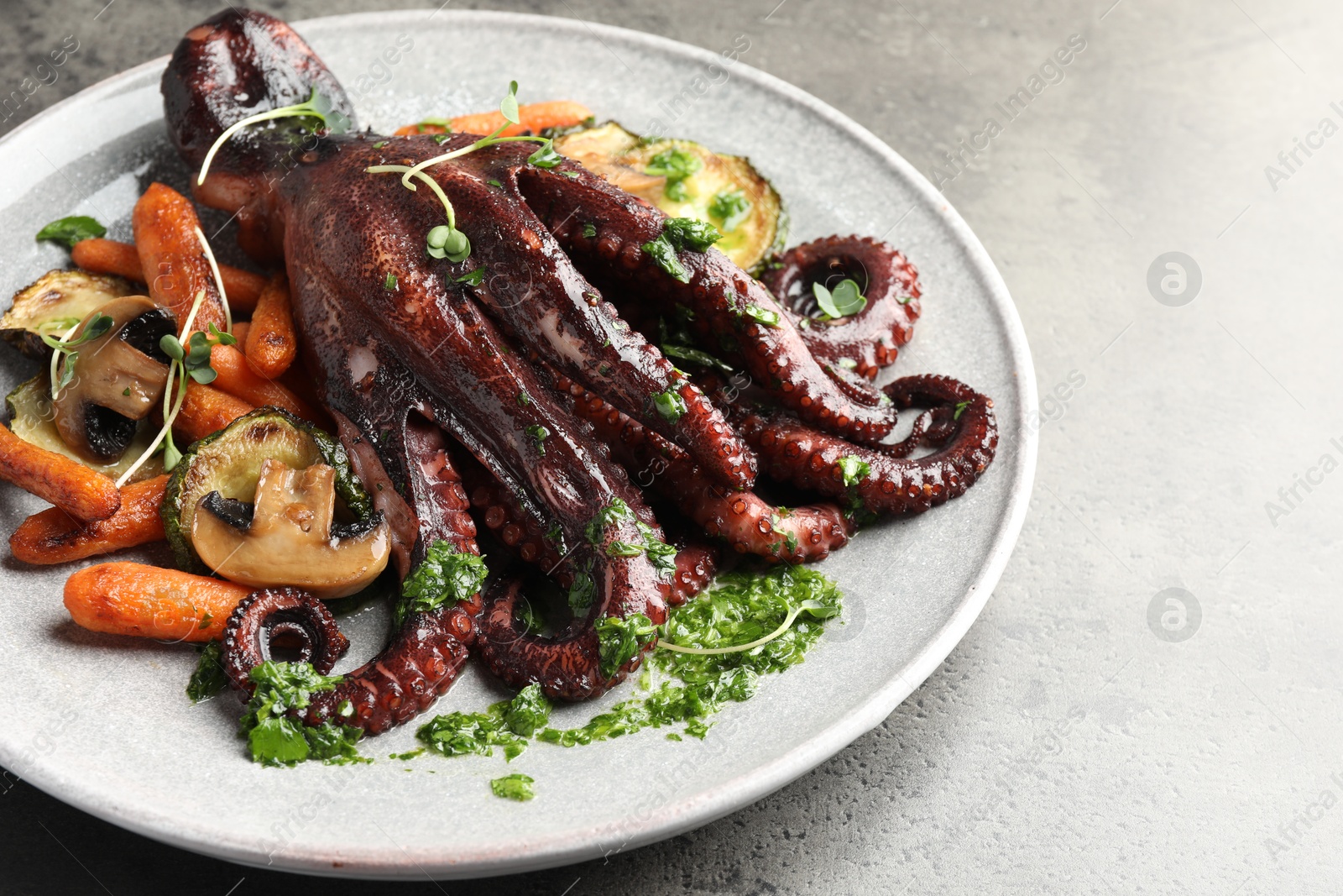 Photo of Roasted octopus with vegetables and mushrooms on grey table, closeup. Space for text