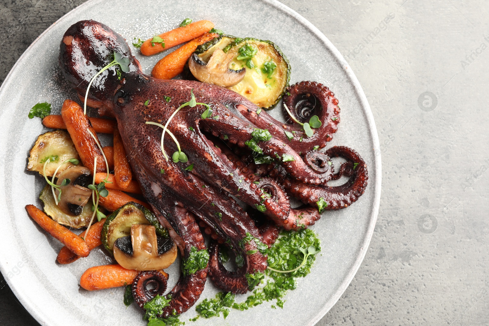 Photo of Roasted octopus with vegetables and mushrooms on grey table, top view. Space for text