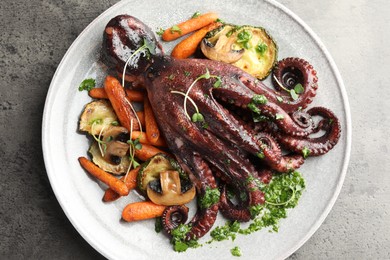 Photo of Roasted octopus with vegetables and mushrooms on grey table, top view