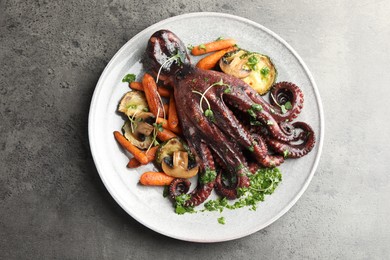 Photo of Roasted octopus with vegetables and mushrooms on grey table, top view