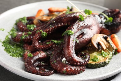 Photo of Roasted octopus with vegetables and mushrooms on table, closeup