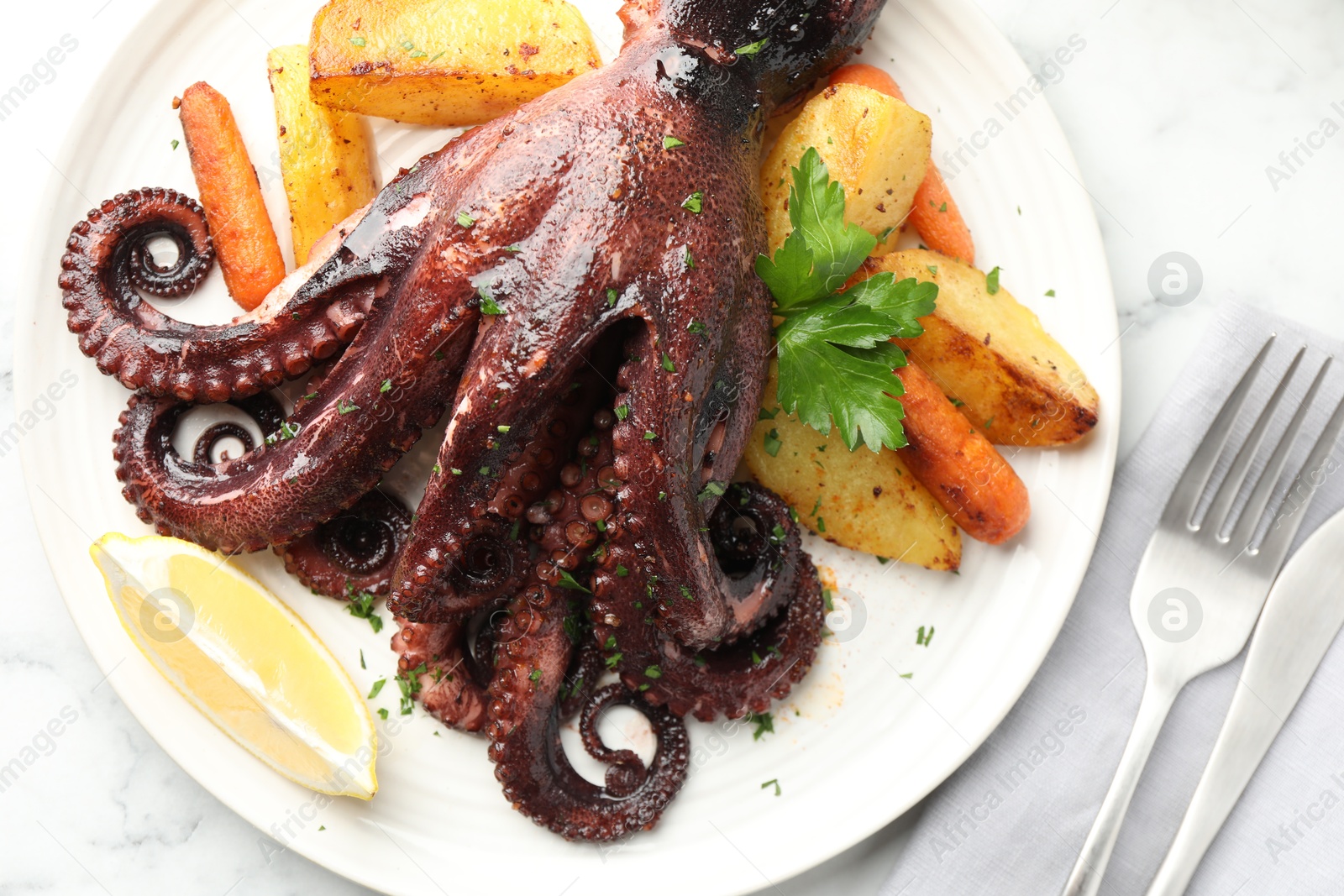 Photo of Roasted octopus with vegetables served on white marble table, flat lay