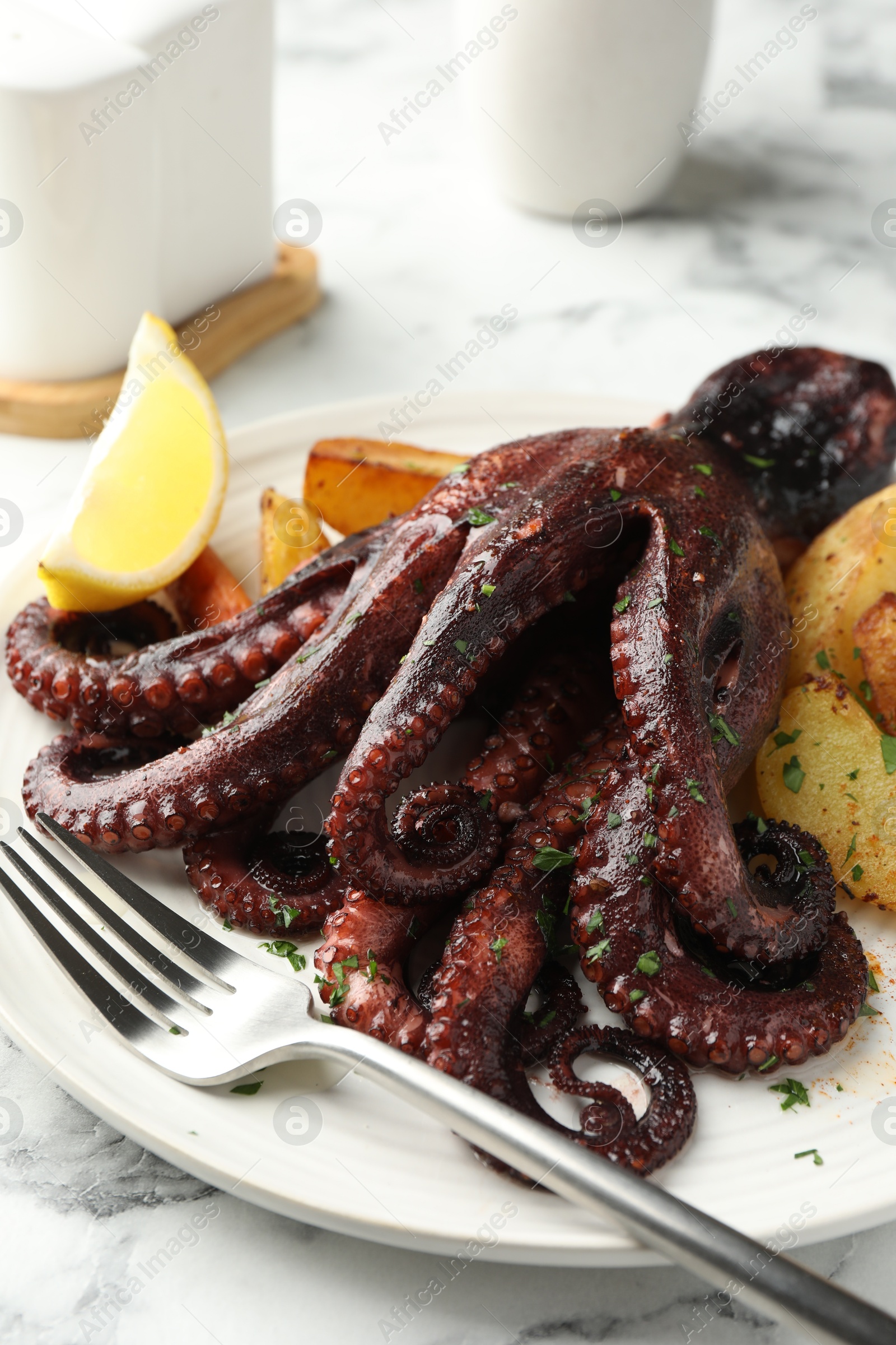 Photo of Roasted octopus with vegetables on white marble table, closeup