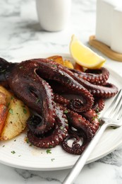 Photo of Roasted octopus with vegetables on white marble table, closeup