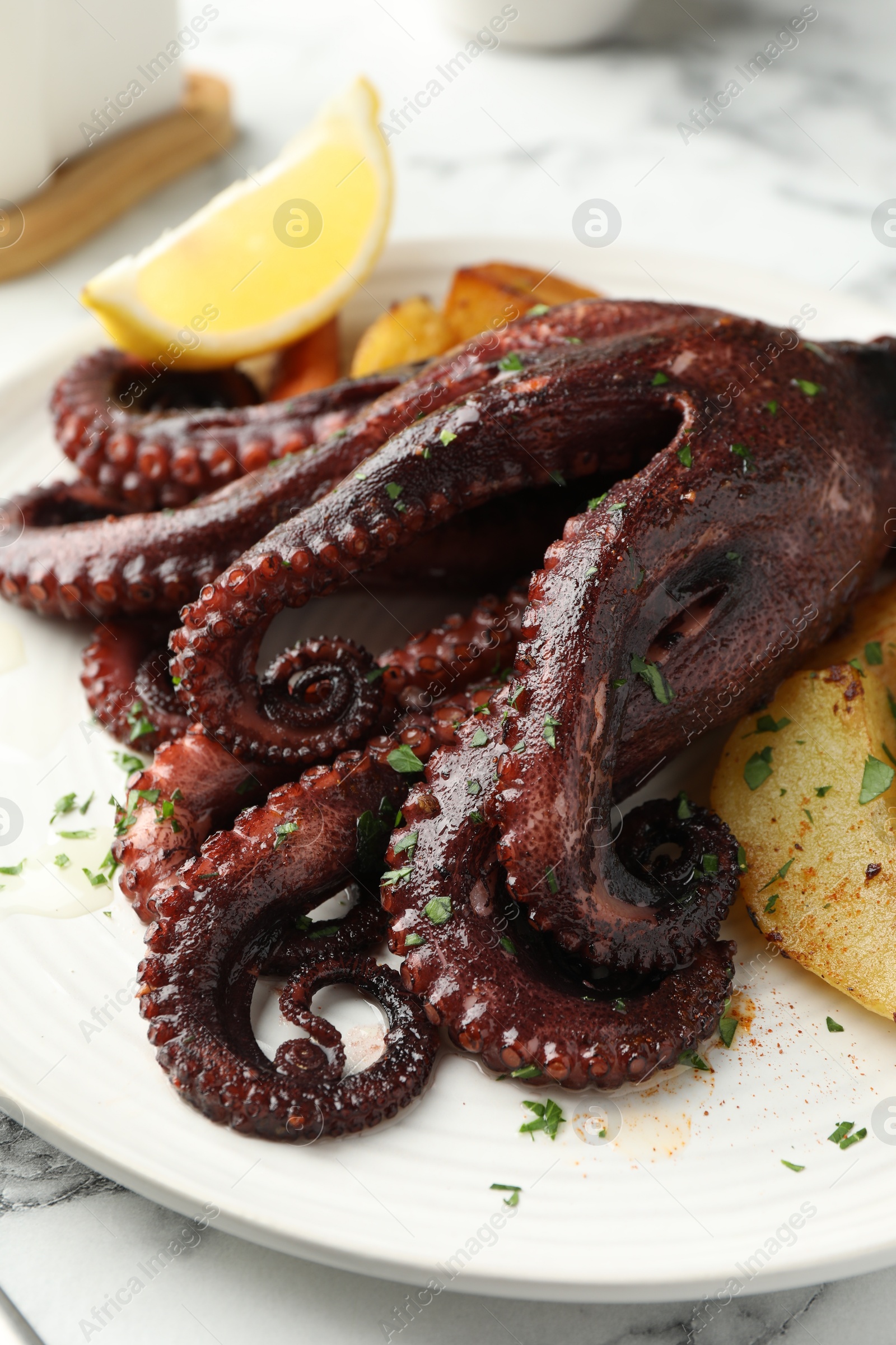 Photo of Roasted octopus with vegetables on white marble table, closeup