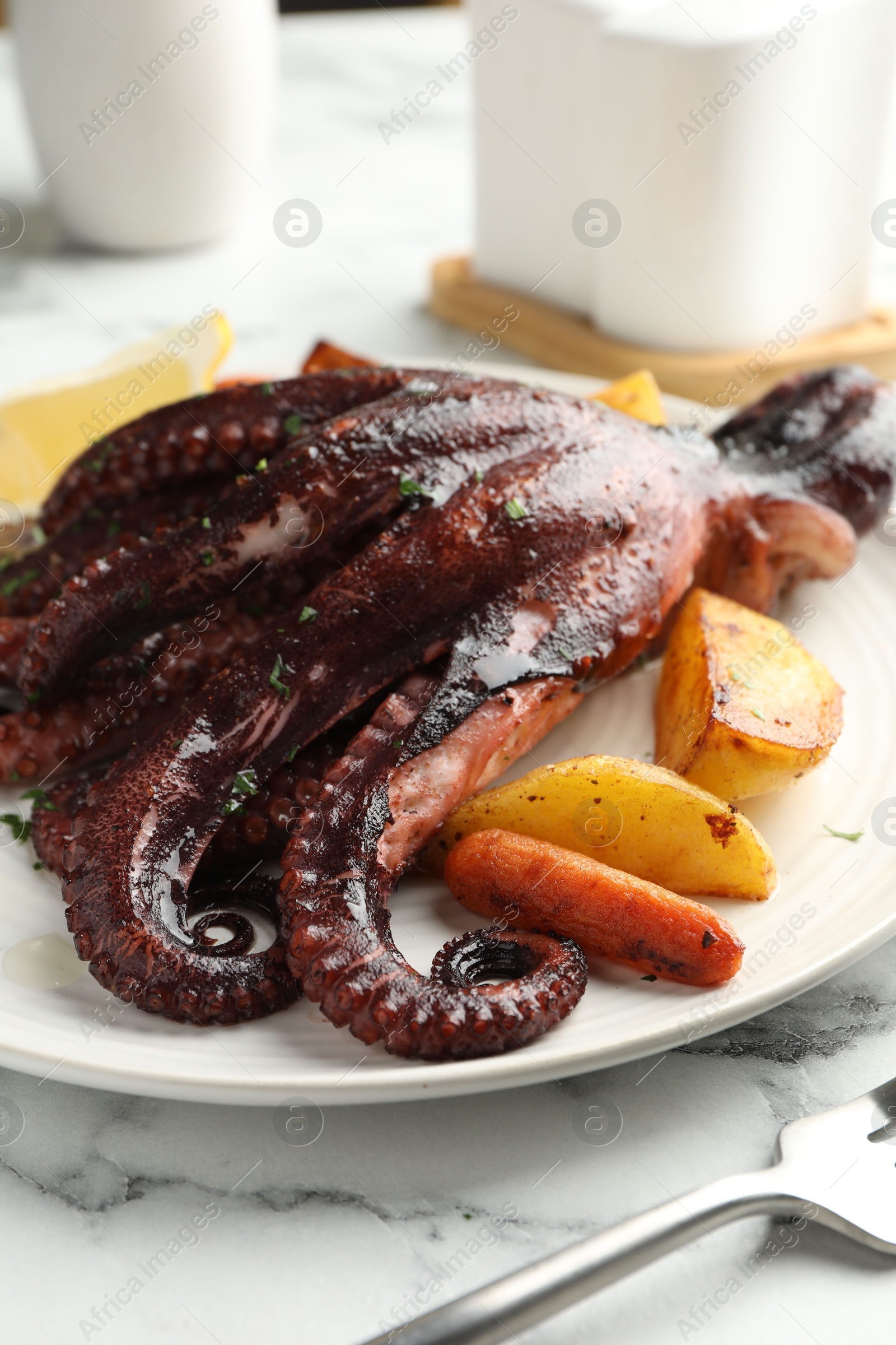 Photo of Roasted octopus with vegetables on white marble table, closeup