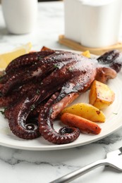 Photo of Roasted octopus with vegetables on white marble table, closeup