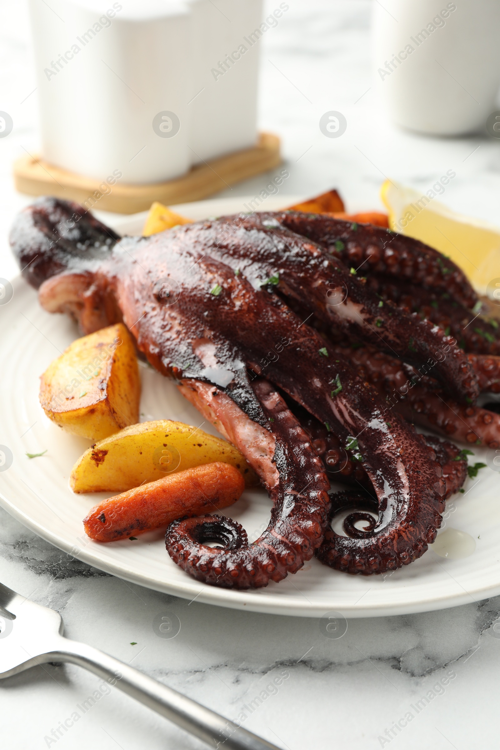 Photo of Roasted octopus with vegetables on white marble table, closeup