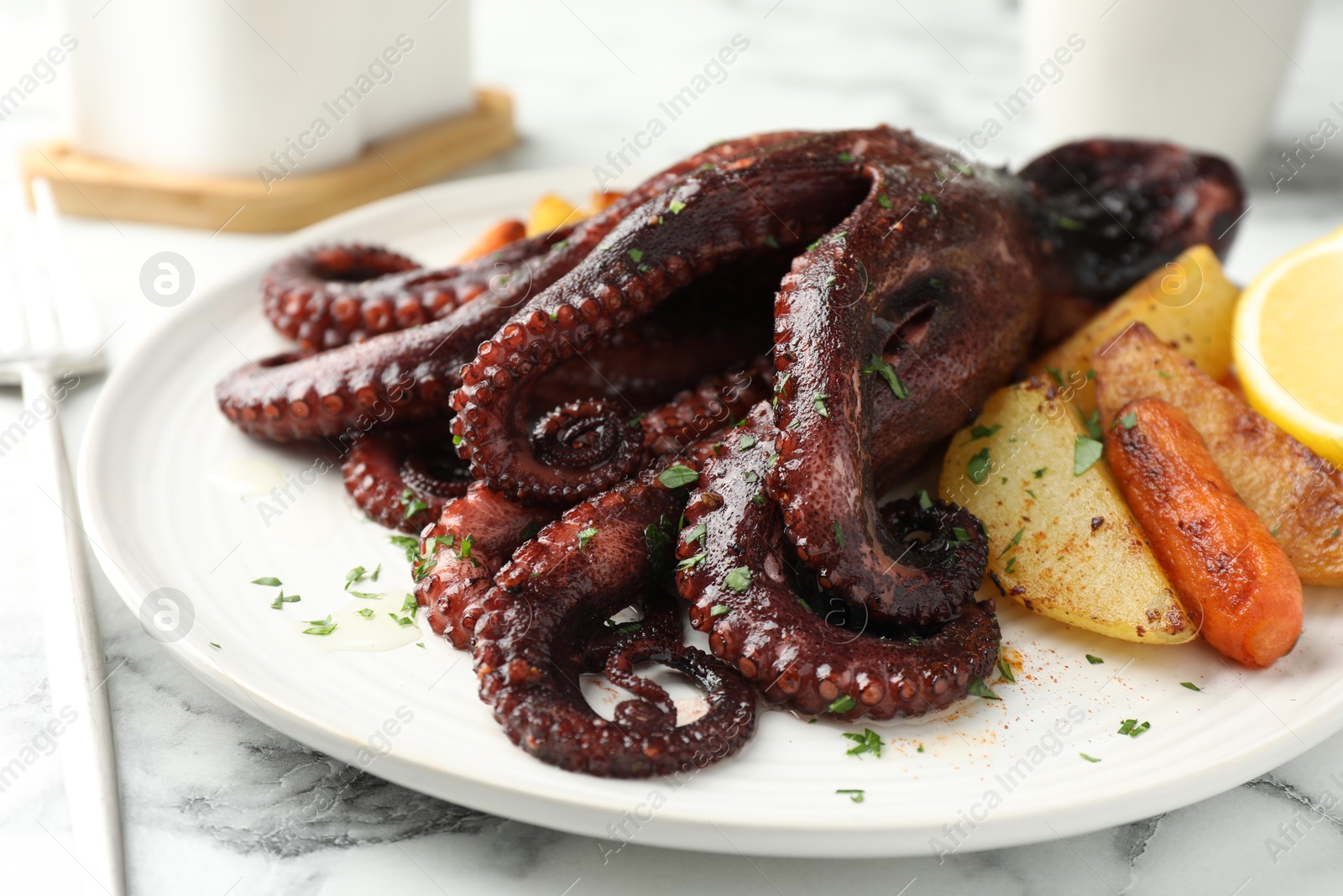 Photo of Roasted octopus with vegetables on white marble table, closeup