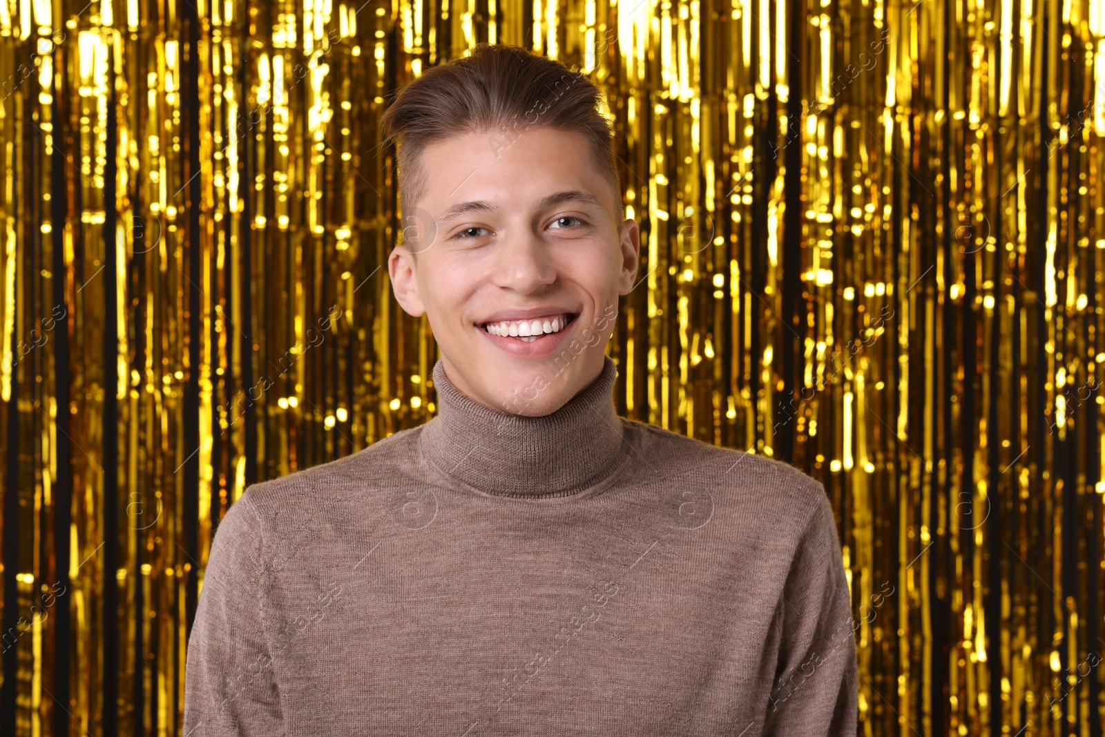 Photo of Happy young man against golden foil curtain