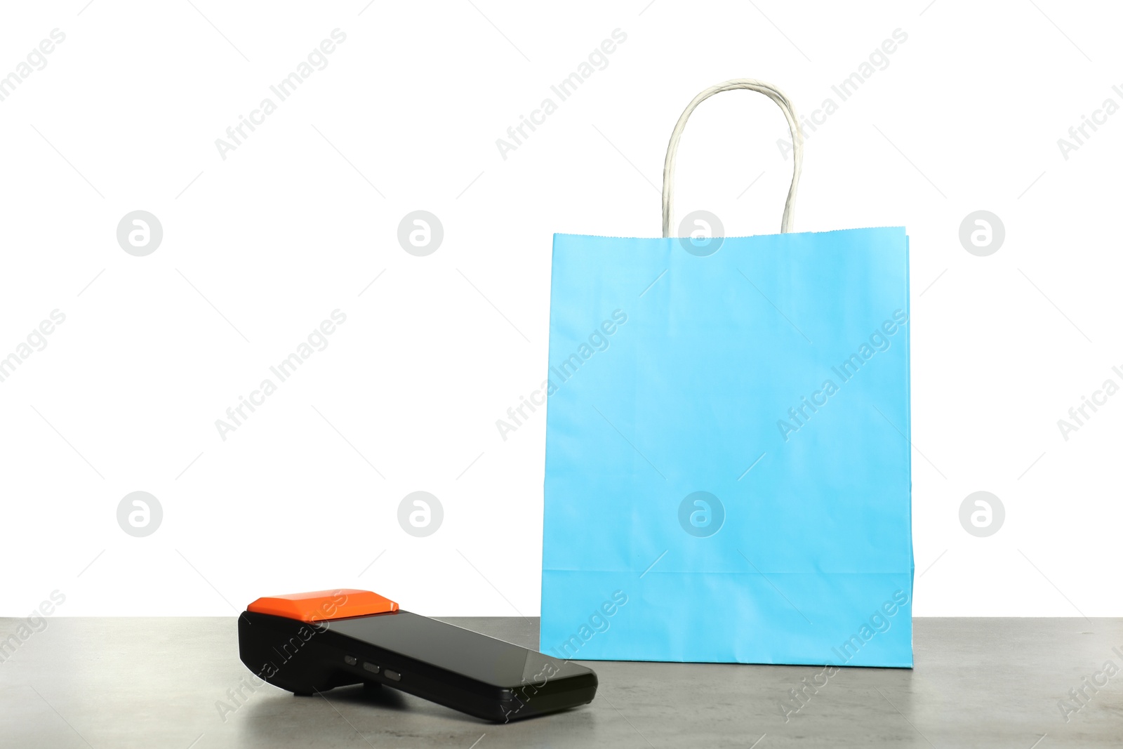 Photo of Payment terminal and shopping bag on grey table against white background