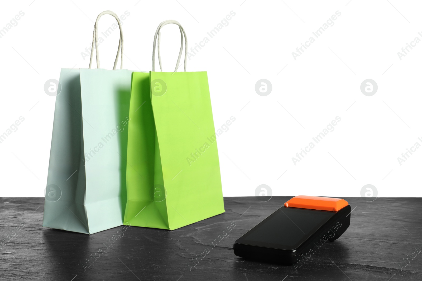 Photo of Payment terminal and shopping bags on black table against white background