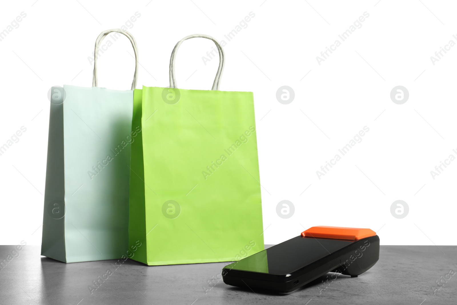 Photo of Payment terminal and shopping bags on grey table against white background