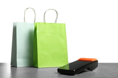 Photo of Payment terminal and shopping bags on grey table against white background