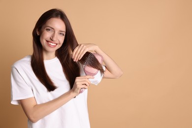 Photo of Smiling woman brushing her hair on beige background, space for text