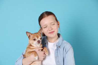 Photo of Teenage girl with her cute Chihuahua dog on light blue background