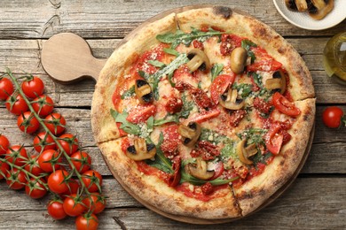 Photo of Tasty pizza with mushrooms, arugula and tomatoes on wooden table, flat lay