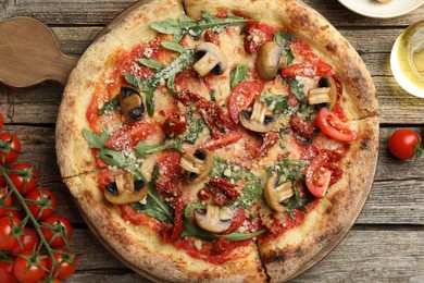 Photo of Tasty pizza with mushrooms, arugula and tomatoes on wooden table, flat lay