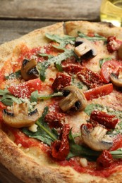 Photo of Tasty pizza with mushrooms, tomatoes and arugula on wooden table, closeup