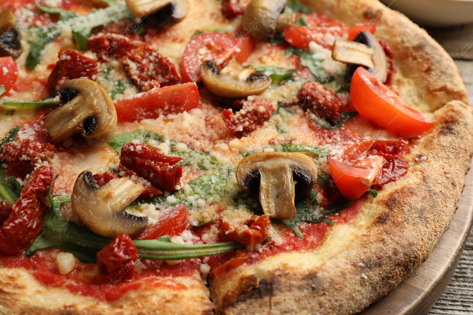 Photo of Tasty pizza with mushrooms, tomatoes and arugula on wooden table, closeup