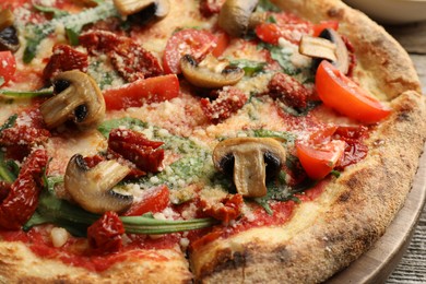 Tasty pizza with mushrooms, tomatoes and arugula on wooden table, closeup