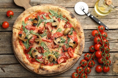 Photo of Tasty pizza with mushrooms, tomatoes, arugula and cutter on wooden table, flat lay