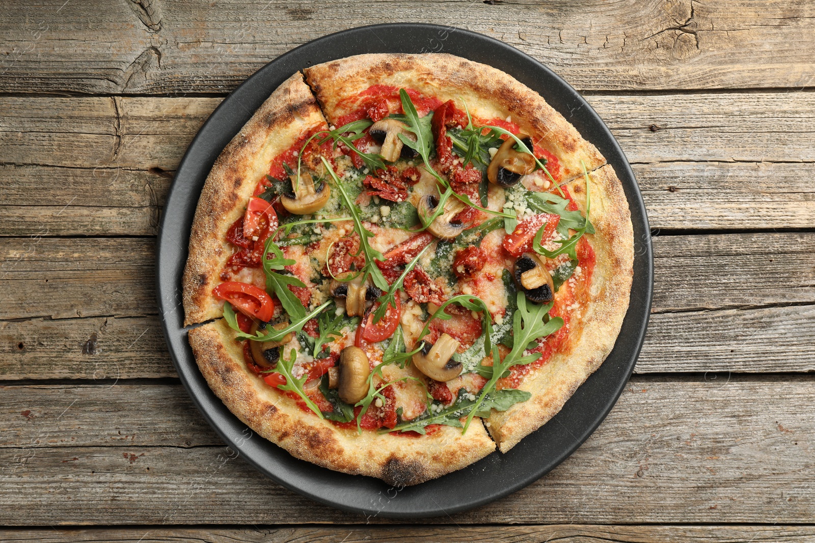 Photo of Tasty pizza with mushrooms, tomatoes and arugula on wooden table, top view