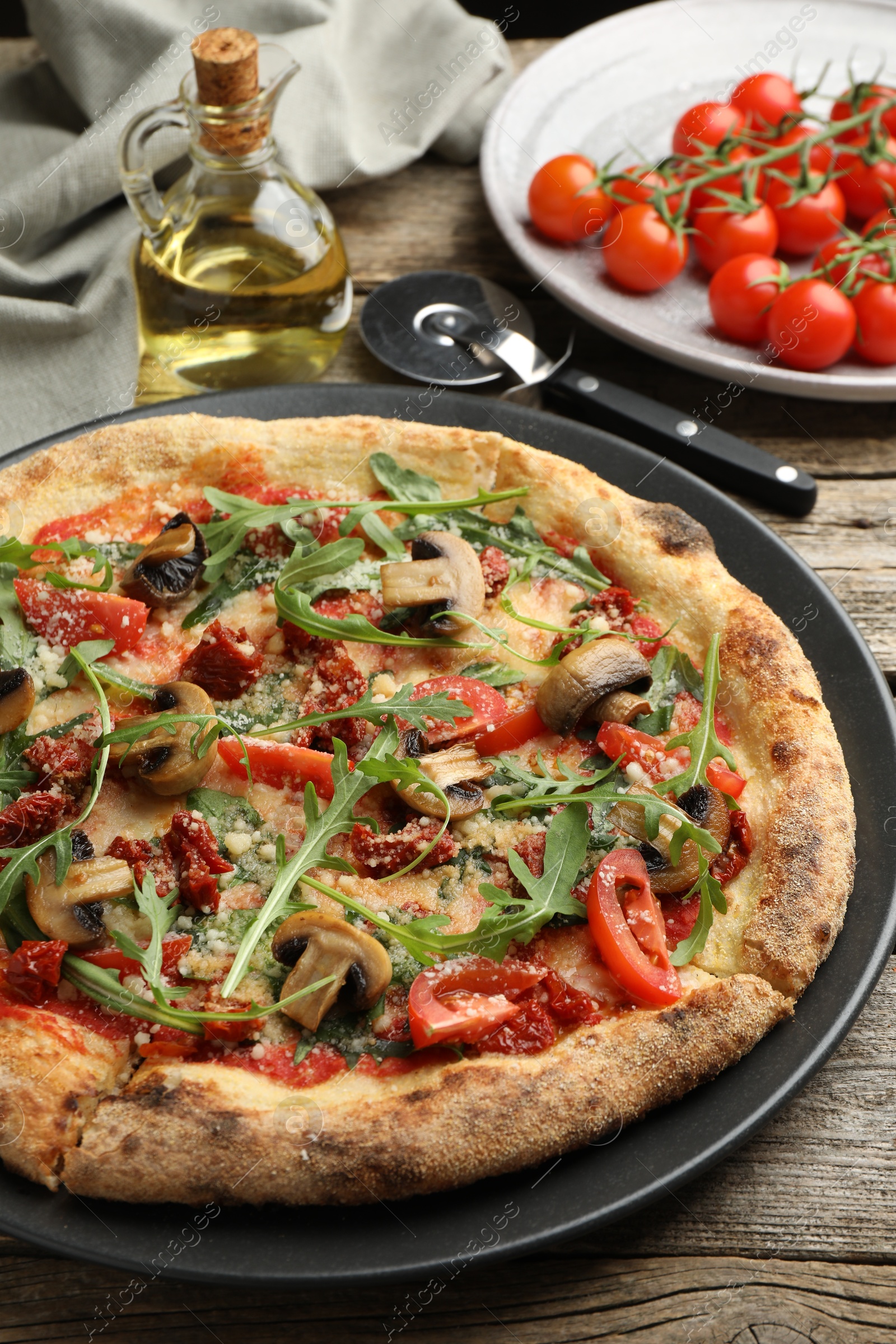 Photo of Tasty pizza with mushrooms, tomatoes and arugula served on wooden table, closeup