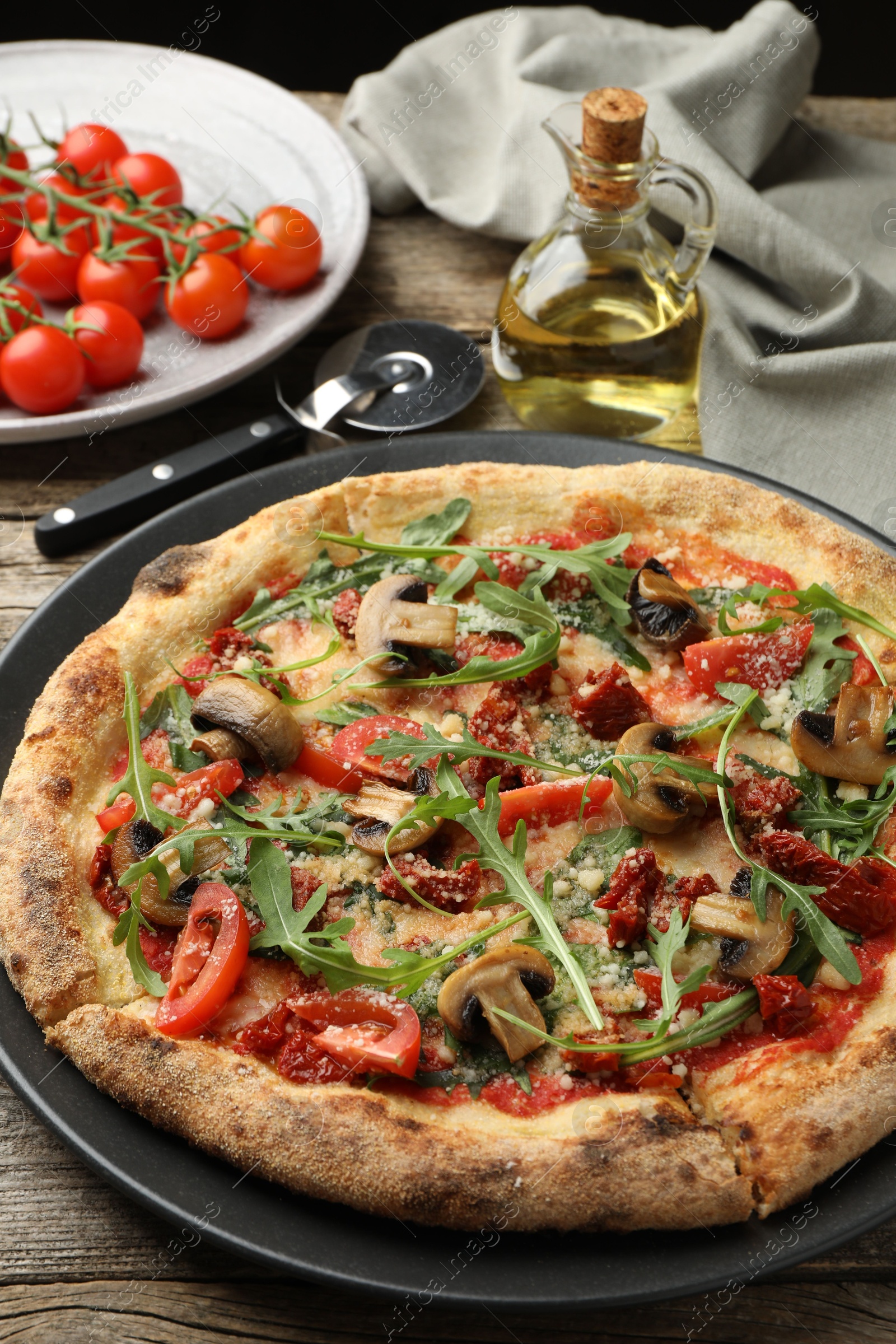 Photo of Tasty pizza with mushrooms, tomatoes and arugula served on wooden table, closeup