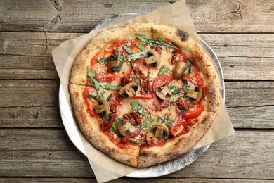 Tasty pizza with mushrooms, tomatoes and arugula on wooden table, top view